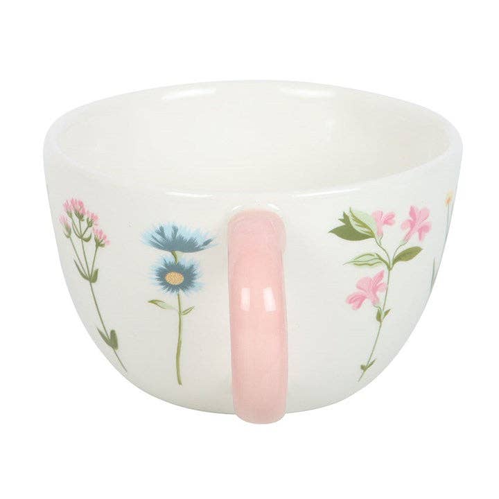 White ceramic mug with a floral pattern and a pink handle.