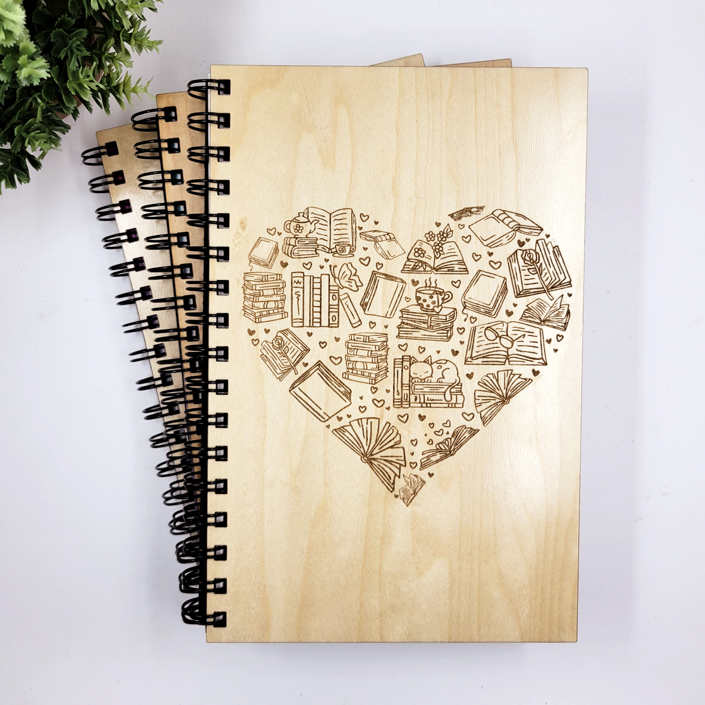 A wood journal with a laser-engraved design in the shape of a heart featuring bookish icons.