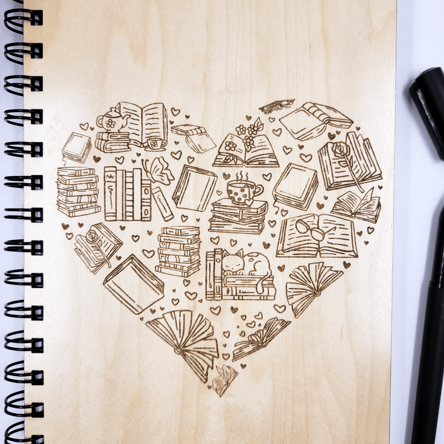 Close up of a wood journal with a laser-engraved design in the shape of a heart featuring bookish icons.