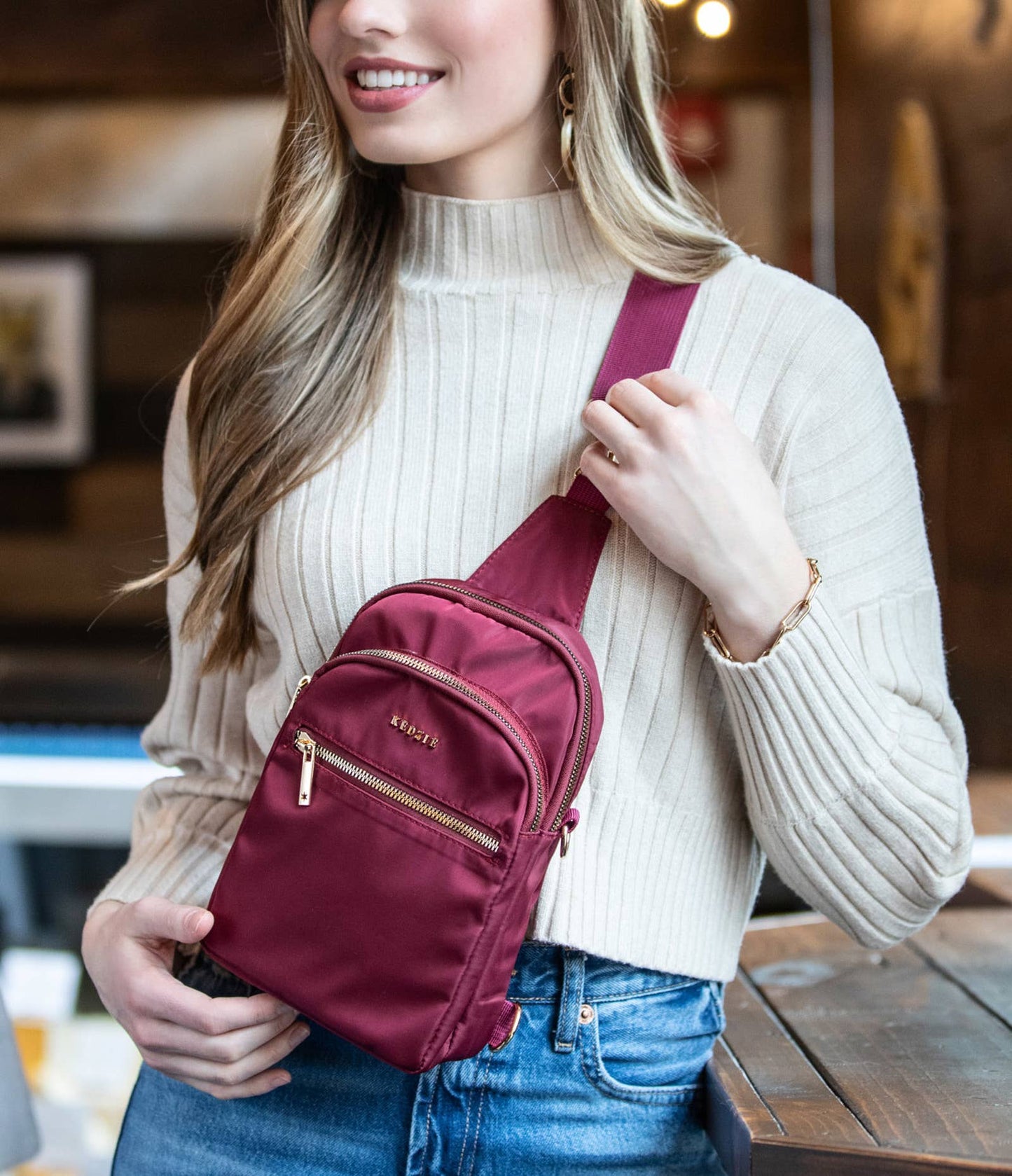Roundtrip convertible sling bag by Kedzie in maroon on a model with a white sweater and jeans.