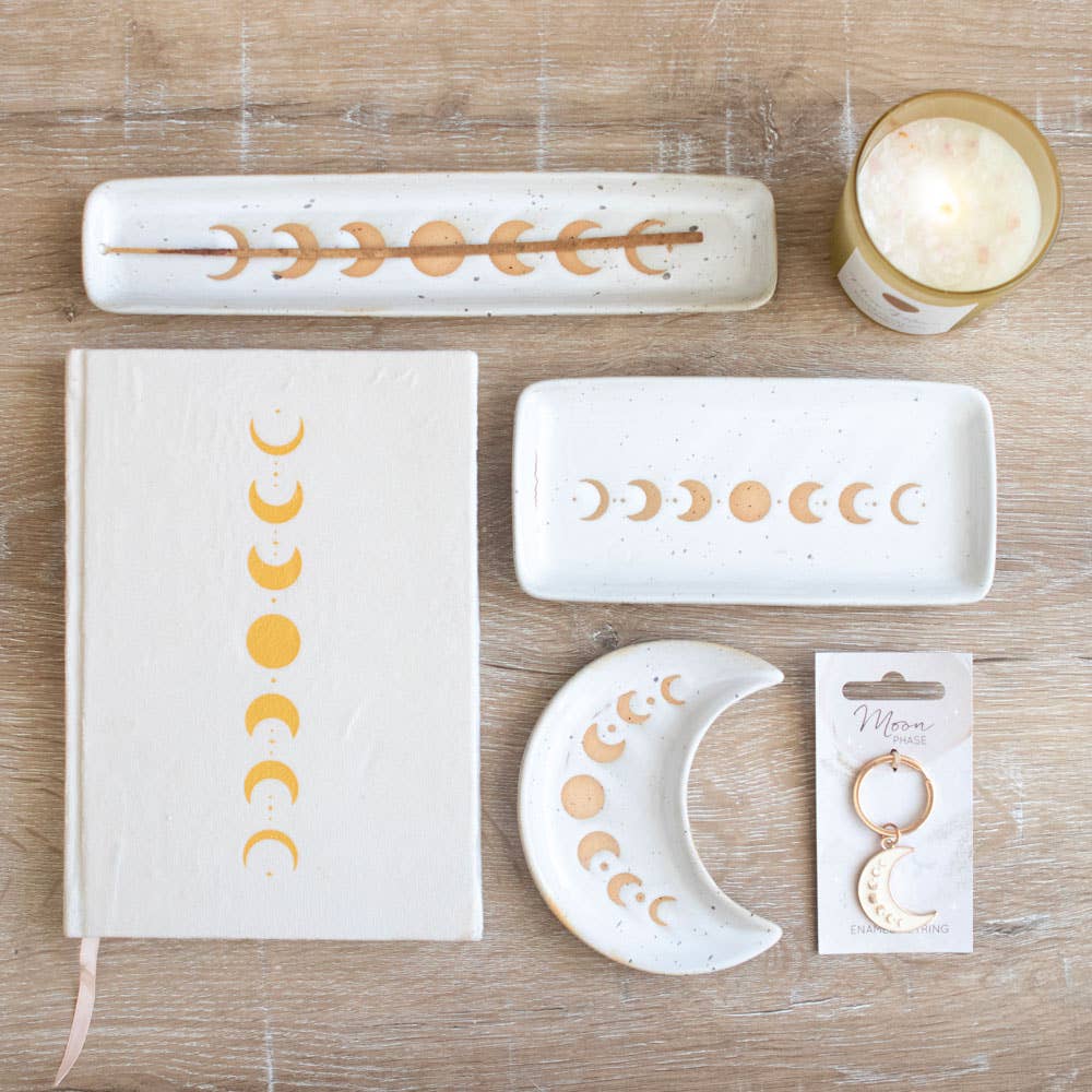 Collection of moon phase items, including a crescent moon keychain. Also pictured for size reference and aesthetics include trinket dishes, incense burner, candle, and notebook.