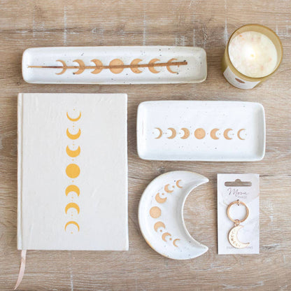 Collection of moon phase items, including a crescent moon keychain. Also pictured for size reference and aesthetics include trinket dishes, incense burner, candle, and notebook.
