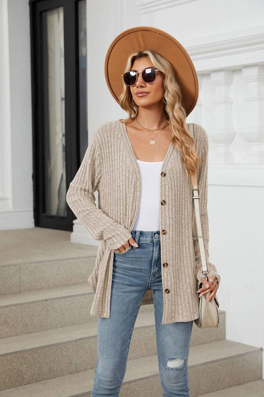 Woman wearing a beige cardigan, blue jeans, and a brown hat outdoors.