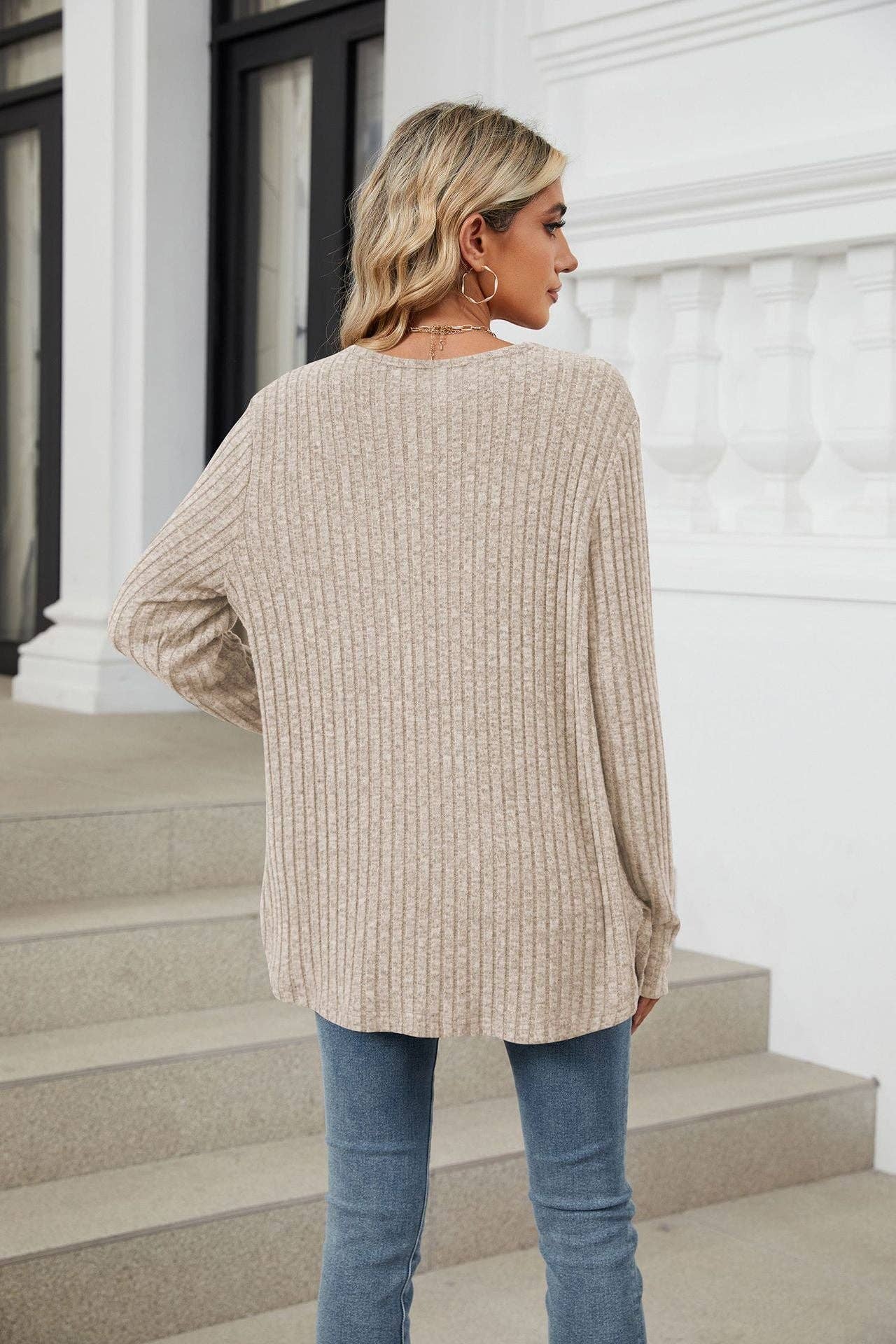 Woman wearing a beige sweater and blue jeans standing on steps with a white building in the background