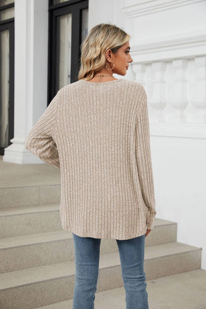 Woman wearing a beige sweater and blue jeans standing on steps with a white building in the background